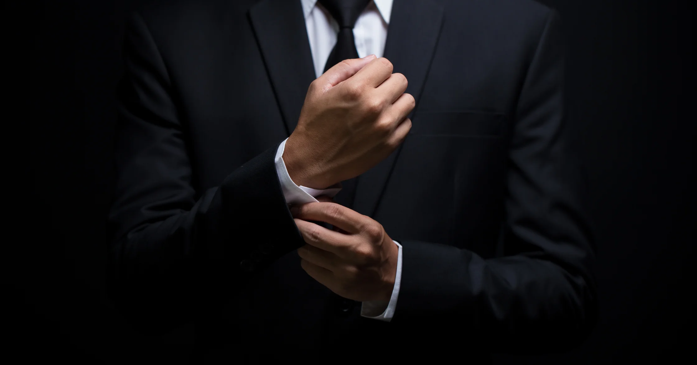 We see a concierge from the neck down in an elegant black suit adjusting his cufflinks.