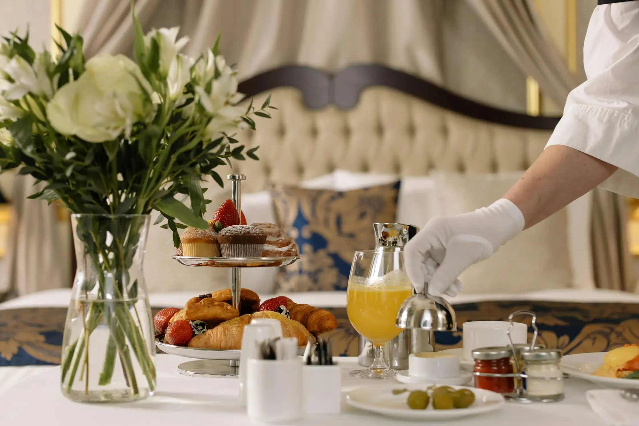 A gloved attendant presents an elegant en-suite room service breakfast.